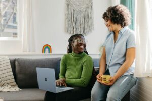 a woman sitting on a couch next to a woman on a laptop
